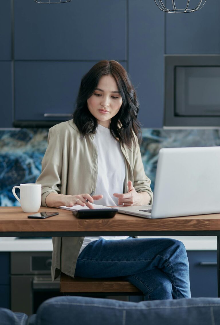 Woman using laptop and calculator at home for finance management.