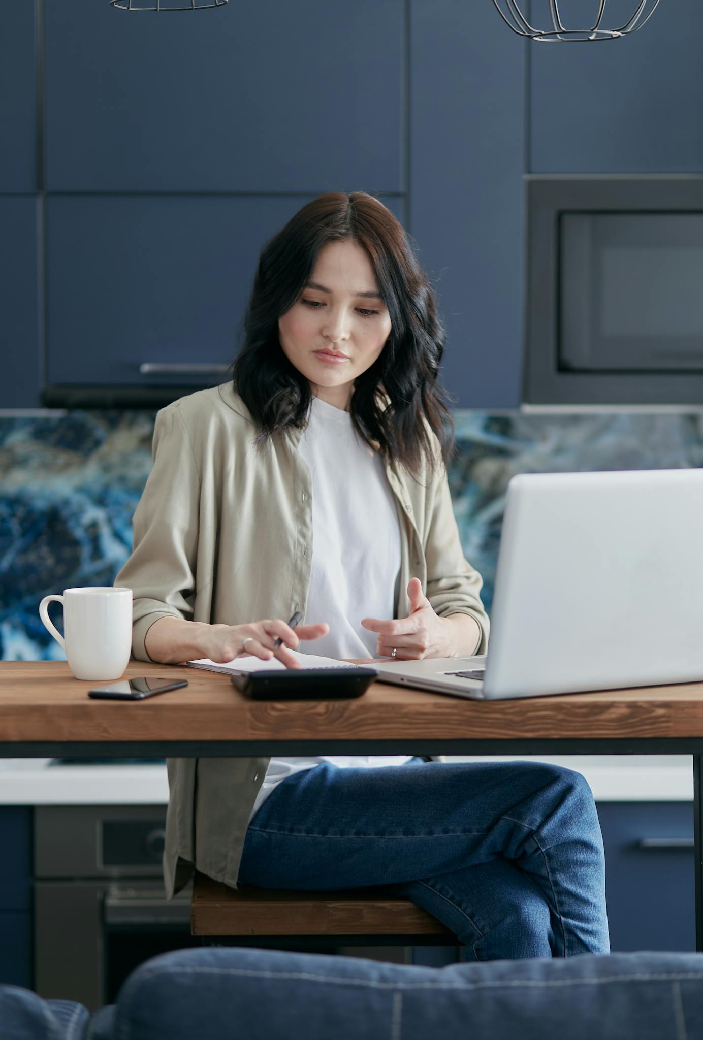 Woman using laptop and calculator at home for finance management.